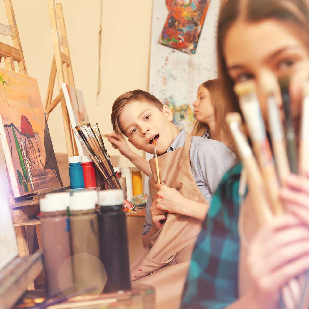 Kids holding paintbrushes in an art studio.